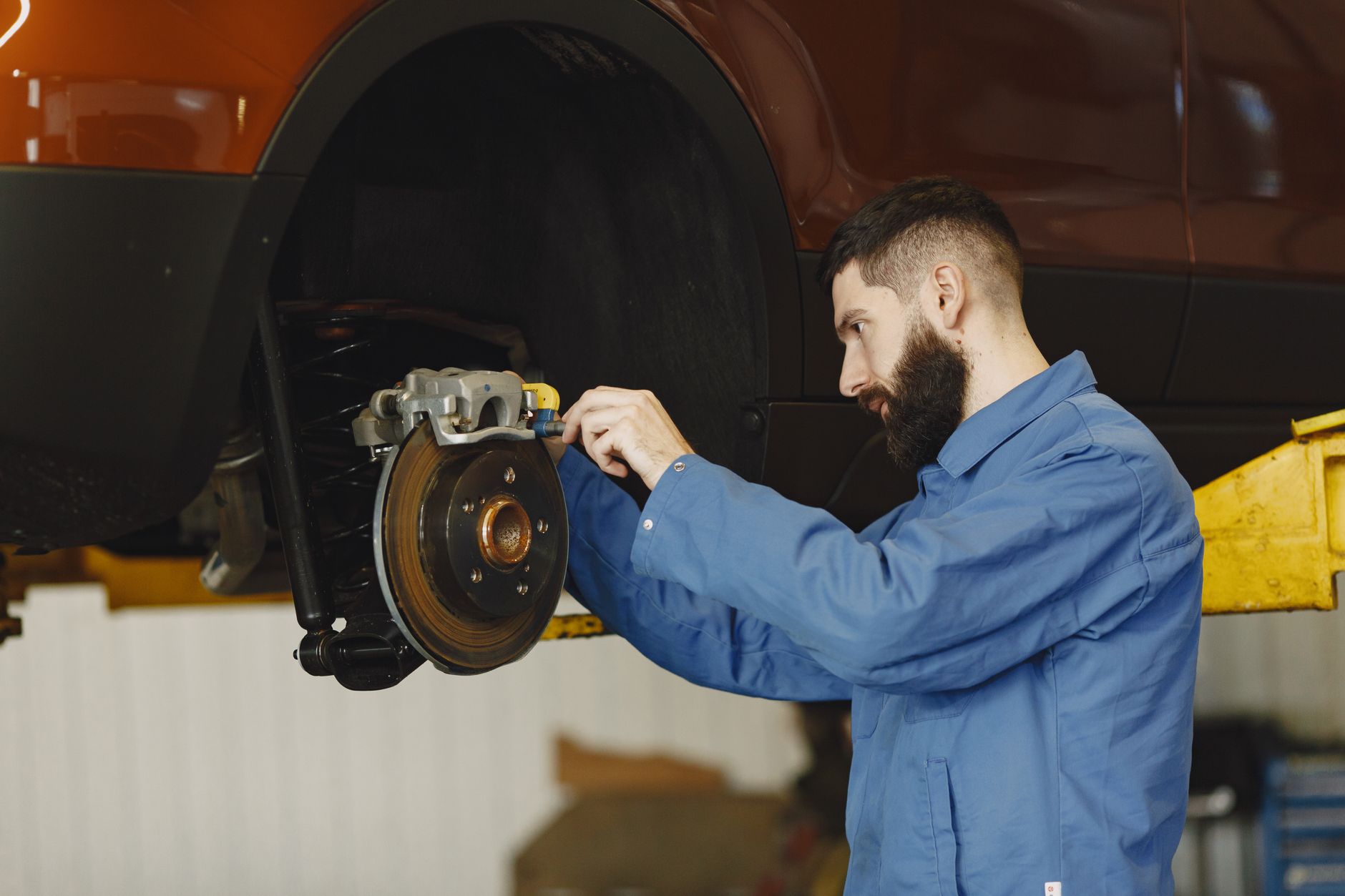 Mechanik w niebieskim kombinezonie naprawia hamulce auta w warsztacie