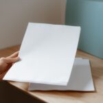 Jak przygotować pliki graficzne do druku i na stronę www: praktyczny przewodnik dla początkujących grafików Osoba trzyma pustą kartkę papieru nad drewnianym biurkiem