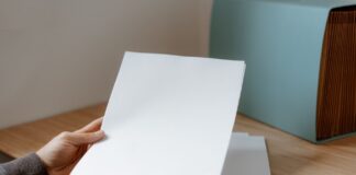 Jak przygotować pliki graficzne do druku i na stronę www: praktyczny przewodnik dla początkujących grafików Osoba trzyma pustą kartkę papieru nad drewnianym biurkiem