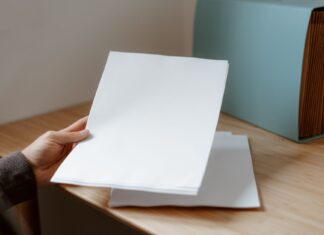 Osoba trzyma pustą kartkę papieru nad drewnianym biurkiem