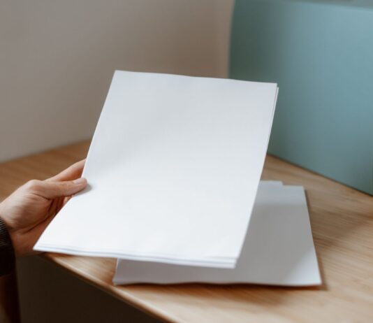 Osoba trzyma pustą kartkę papieru nad drewnianym biurkiem