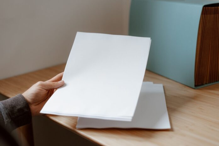 Osoba trzyma pustą kartkę papieru nad drewnianym biurkiem Osoba trzyma pustą kartkę papieru nad drewnianym biurkiem
