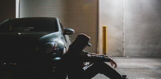 Zmęczony kierowca siedzi na asfalcie oparty o zaparkowane auto o zmierzchu