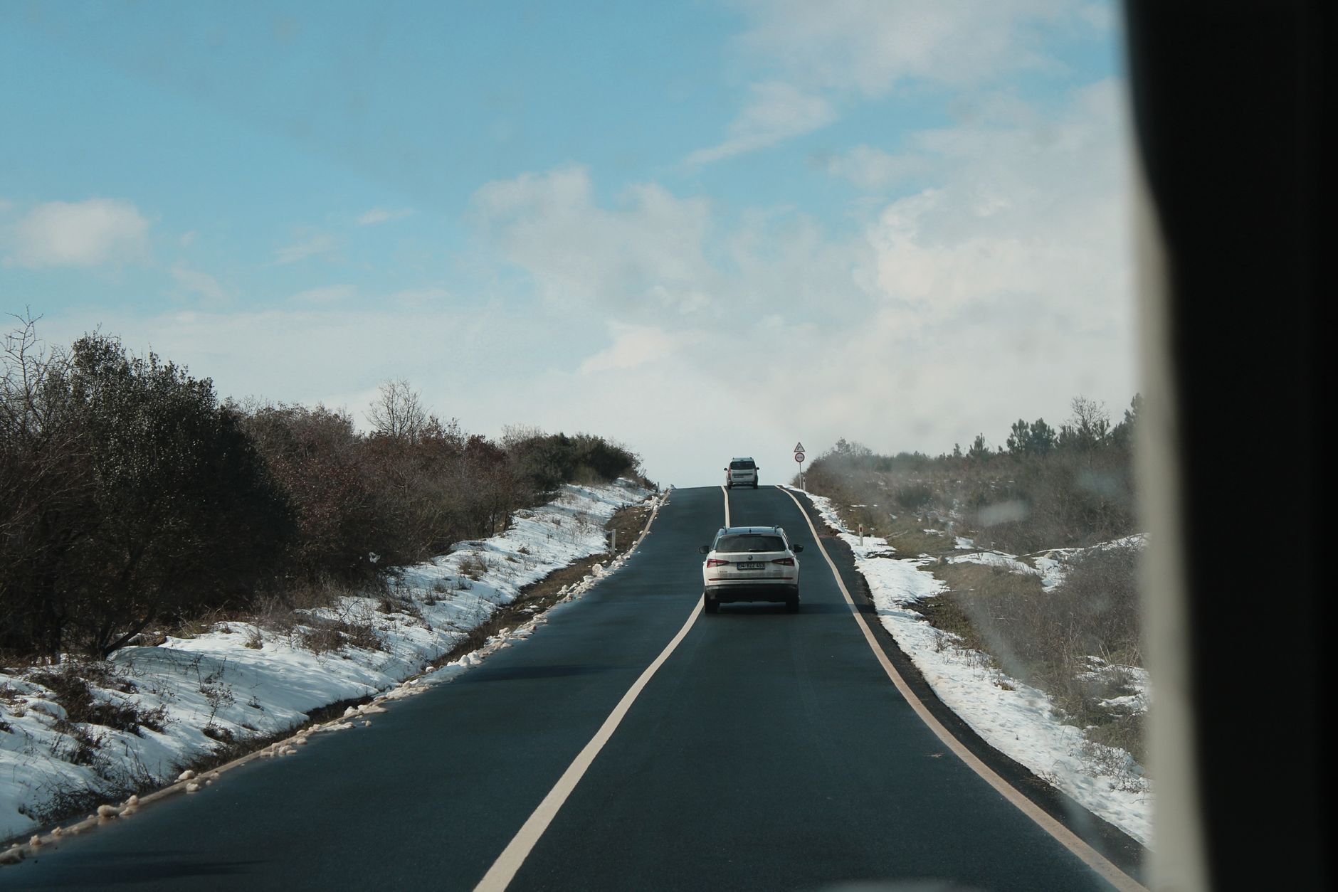 Samochody jadą zaśnieżoną wiejską drogą wśród drzew